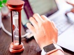 Песочные часы рядом с рукой на клавиатуре ноутбука