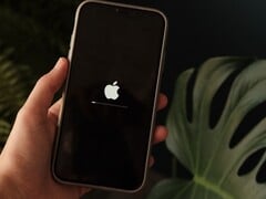 На экране видна рука, держащая iPhone; на экране светятся логотип Apple и индикатор выполнения.