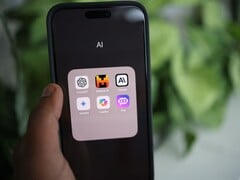 Рука держит смартфон, на экране которого видна папка с названием «AI», содержащая приложения Gemini, ChatGPT и Claude