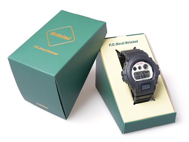 Часы Casio G-Shock x F.C. Real Bristol DW-6900 представлены в зеленой коробке с совместным брендингом, а рядом с ними — соответствующий внешний чехол.