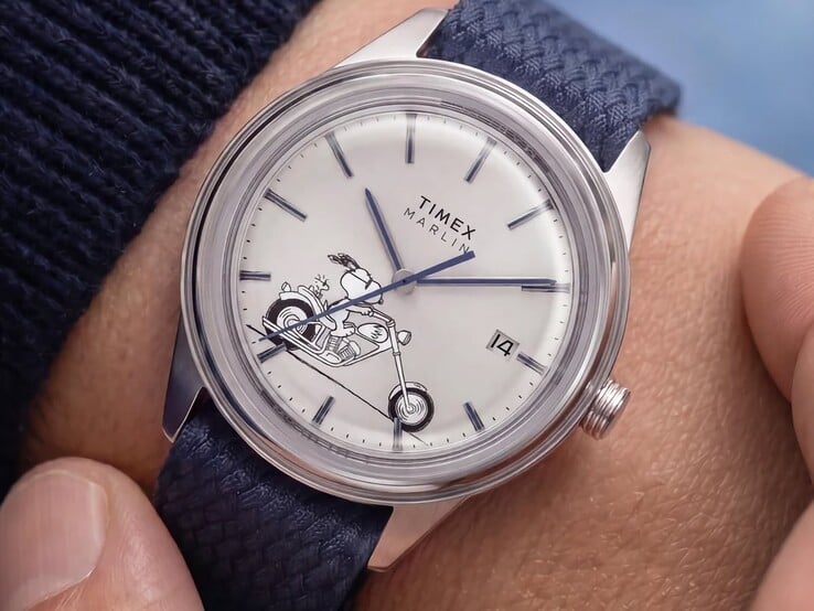 Часы Peanuts x Timex Marlin Jet Automatic Easy Rider на запястье, на серебристо-белом циферблате которых изображён Снупи, едущий на мотоцикле, с синими индексами и стрелками, а также синий ремешок из тканого материала.