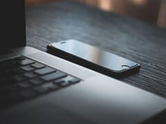 Смартфон, лежащий рядом с открытым ноутбуком на тёмном столе