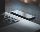 Смартфон, лежащий рядом с открытым ноутбуком на тёмном столе