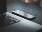 Смартфон, лежащий рядом с открытым ноутбуком на тёмном столе