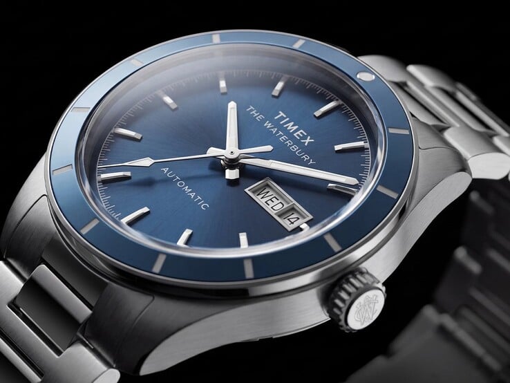 Крупный план часов Timex Waterbury Heritage Automatic с синим циферблатом, на котором видны светящиеся стрелки, накладные часовые метки и индикатор дня недели и даты.