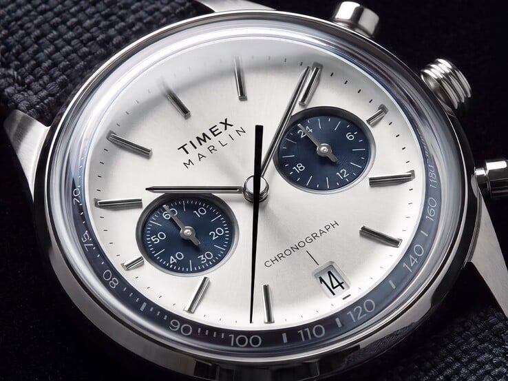 Крупный план хронографа Timex Marlin Jet TW2Y89900 с серебристо-белым циферблатом, темно-синими вспомогательными циферблатами, накладными часовыми метками, стрелками в форме палочек, тахиметрической шкалой и окошком даты.