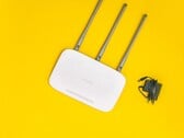 Белый Wi-Fi-роутер с тремя антеннами и блоком питания на желтом фоне