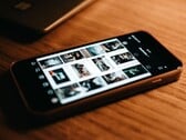 Смартфон, лежащий на деревянном столе; на его экране отображается сетка фотографий