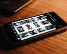 Смартфон, лежащий на деревянном столе; на его экране отображается сетка фотографий