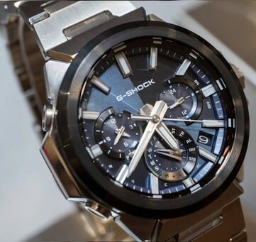 Крупный план часов Casio G-Shock GST-W1000AD-2A с синим циферблатом, на котором видны трёхслойная компоновка с тремя дополнительными циферблатами, светящиеся метки, серебристые стрелки и чёрный безель.
