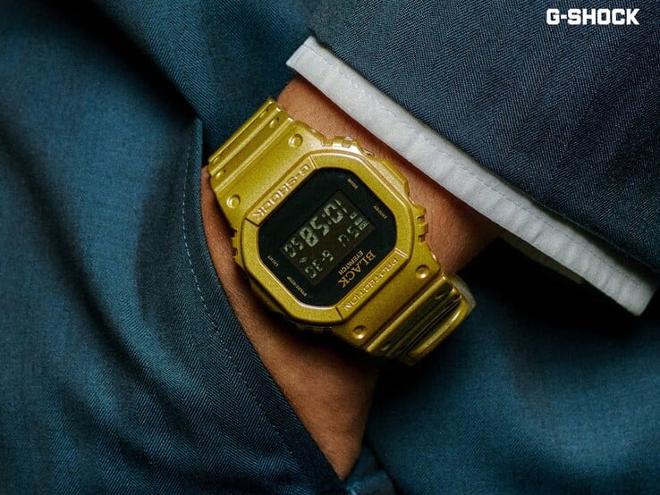 Крупный план золотых часов Casio G-Shock DW-5600BEP-9, надетых на запястье на фоне тёмно-синей ткани. Часы имеют чёрный цифровой дисплей, золотой корпус и ремешок, а также логотип BlackEyePatch на безеле и циферблате.