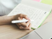 Человек делает записи в блокноте, сидя рядом с открытым ноутбуком