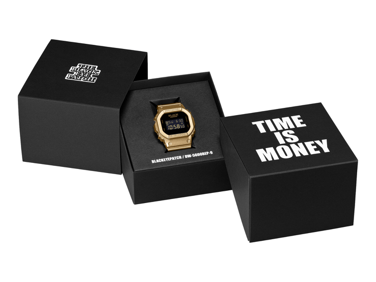 Золотые часы Casio G-Shock DW-5600BEP-9 с чёрным цифровым дисплеем расположены между двумя чёрными презентационными коробками. На циферблате часов размечёно логотип BlackEyePatch, а на коробке на переднем плане написано: «ВРЕМЯ — ЭТО ДЕНЬГИ».