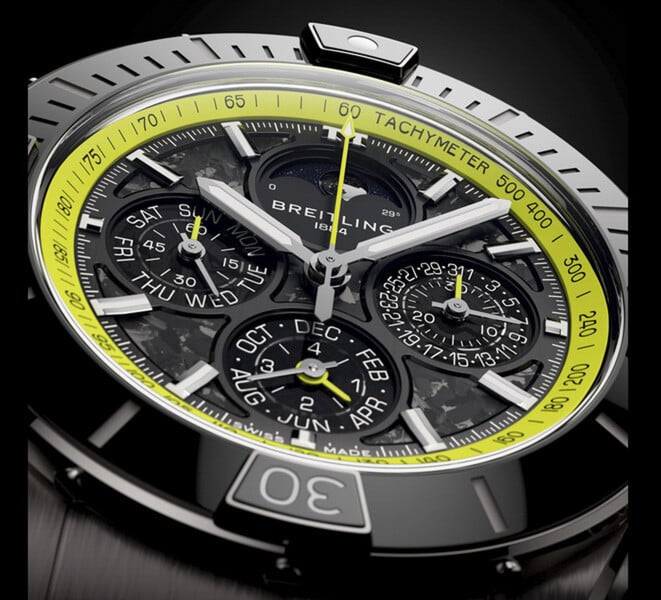 Крупный план Breitling Super Chronomat B19 44 Perpetual Calendar Chronograph: циферблат из углеродного волокна, дополнительные циферблаты календаря, серебристые стрелки и лаймово-зелёная тахиметрическая шкала.