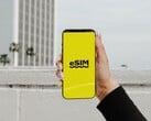 Рука, держащая смартфон с крупно отображённым словом «eSIM» на жёлтом экране.