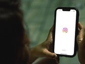 Женщина, держащая смартфон обеими руками; на экране отображается стартовый экран Instagram