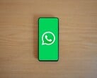Смартфон на деревянном столе с зелёным стартовым экраном приложения WhatsApp и его логотипом.