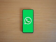 Смартфон на деревянном столе с зелёным стартовым экраном приложения WhatsApp и его логотипом.