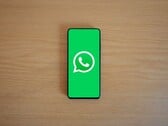 Смартфон на деревянном столе с зелёным стартовым экраном приложения WhatsApp и его логотипом.